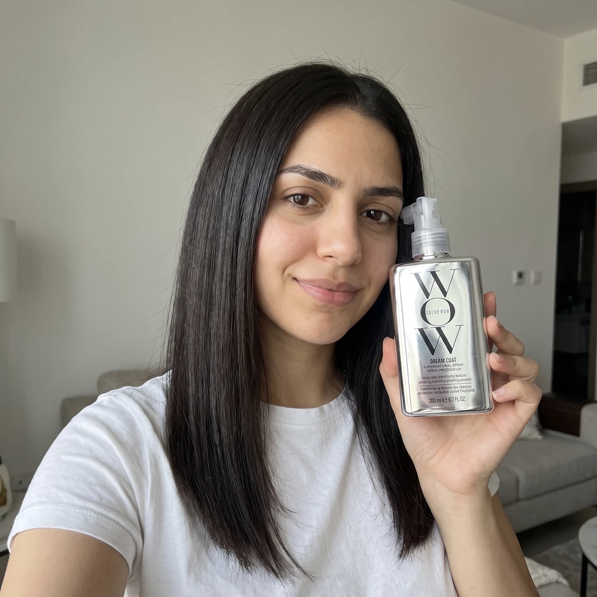امرأة مبتسمة تمسك بخاخ Color Wow Dream Coat وشعرها ناعم